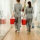 Back view of two custodial staff walking down a hallway carrying buckets