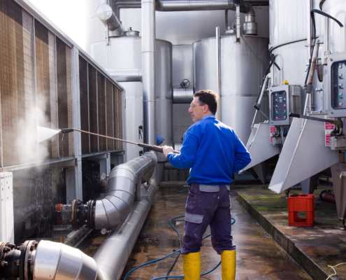 Side view of a man power washing industrial equipment